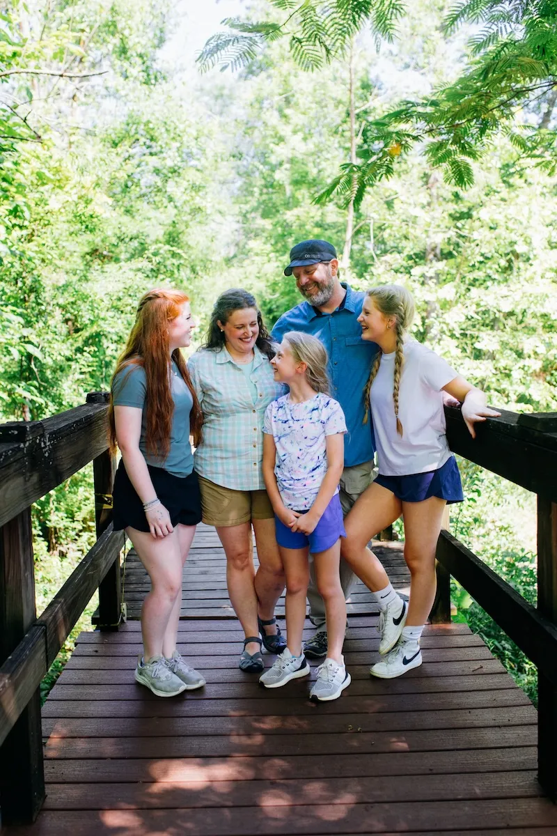 Family standing together on a wooden bridge surrounded by trees
